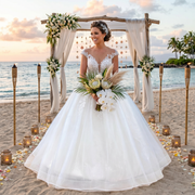 Smiling bride on a beach at sunset holding a tropical bouquet, wearing a luxury cap sleeve vintage wedding dress featuring a full tulle skirt and 3D handmade flowers.