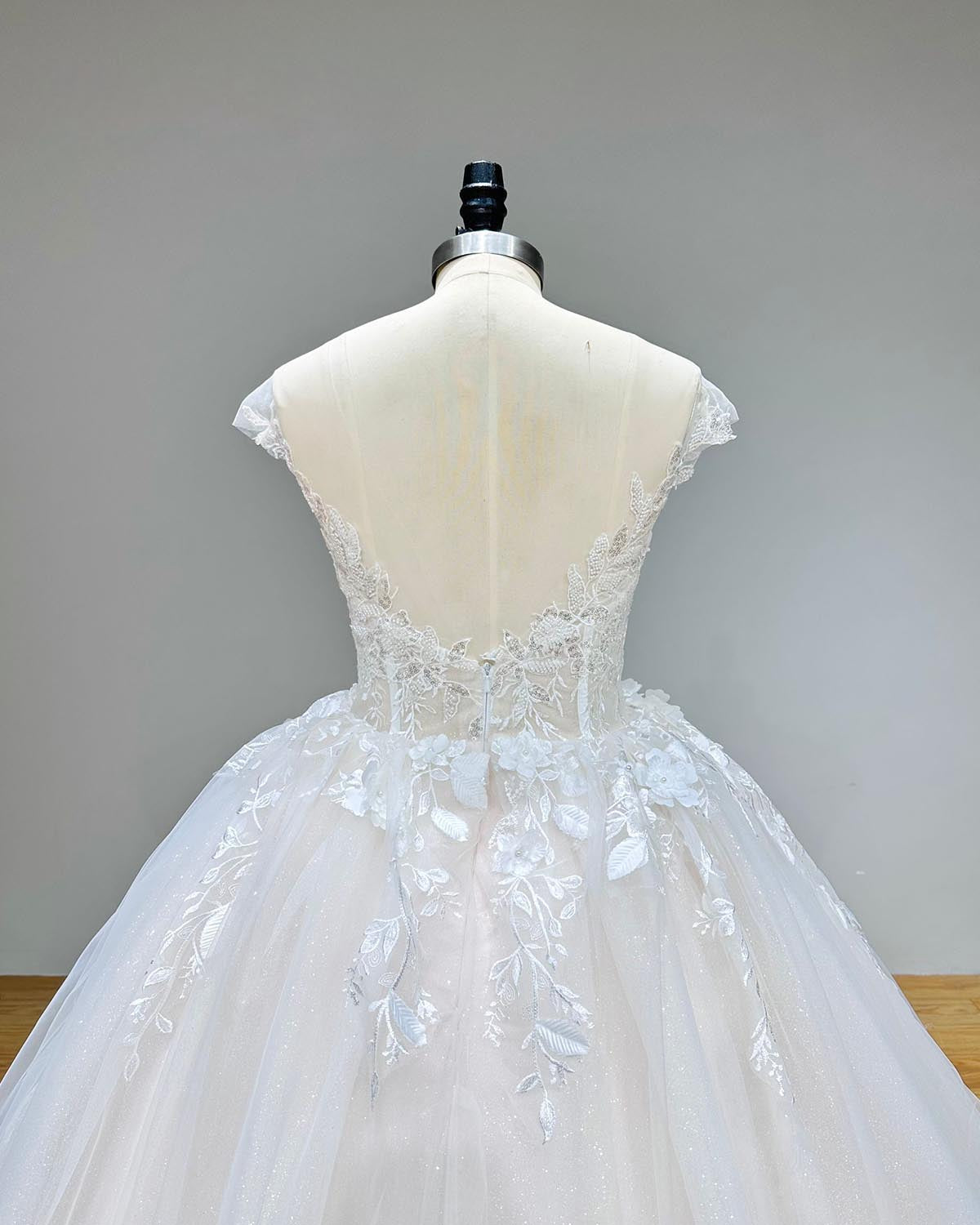 Close-up back view of a luxury vintage wedding dress on a mannequin, detailing the sheer backless design, delicate cap sleeves, and 3D handmade floral lace at the waistline.