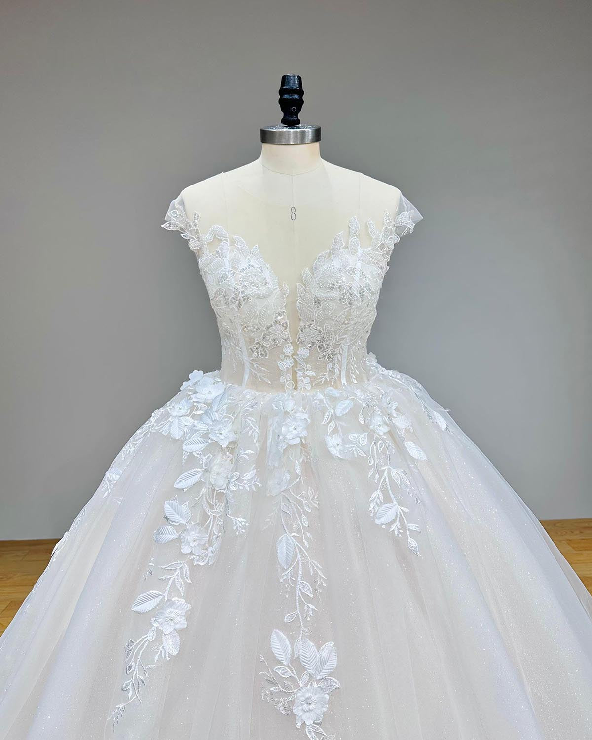 Close-up front bodice view of a luxury cap sleeve vintage wedding dress, featuring an illusion plunging neckline heavily embellished with 3D handmade flowers and subtle sequin beading.