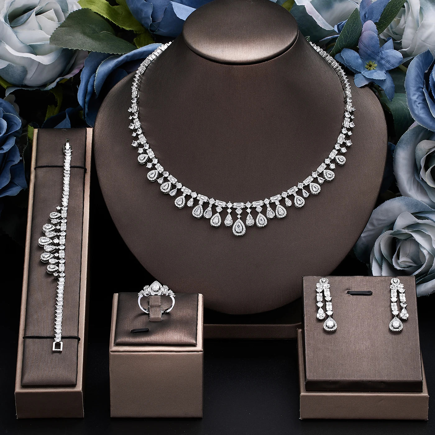 Complete 4-piece cubic zirconia bridal jewelry set with crystal accents, displaying a halo teardrop collar necklace, bracelet, ring, and earrings on brown display stands.