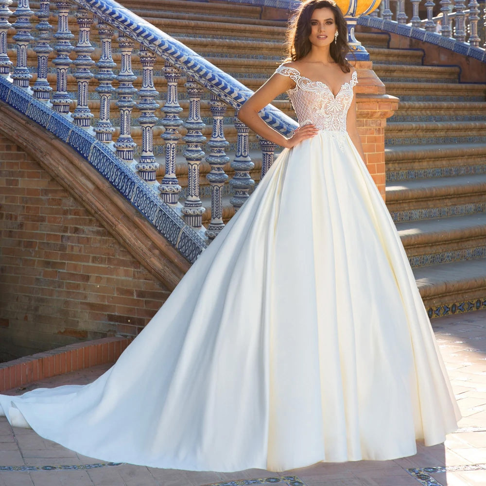 A beautiful bride standing on a stone terrace, wearing an off-the-shoulder A-line wedding dress with long sleeves and delicate lace appliques.