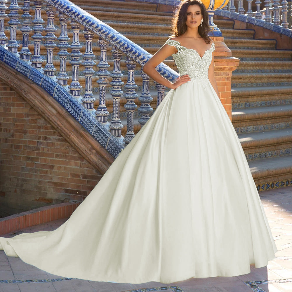 Close-up of a bride in an elegant off-the-shoulder wedding gown, highlighting the detailed lace applique on the long sleeves and bodice.