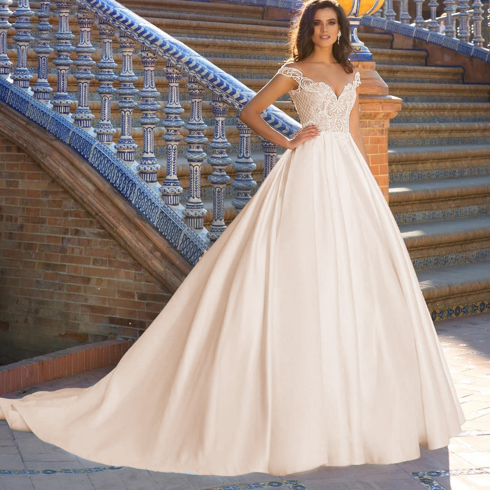A bride posing gracefully in a vintage-inspired off-the-shoulder wedding dress with long lace sleeves and intricate floral appliques.