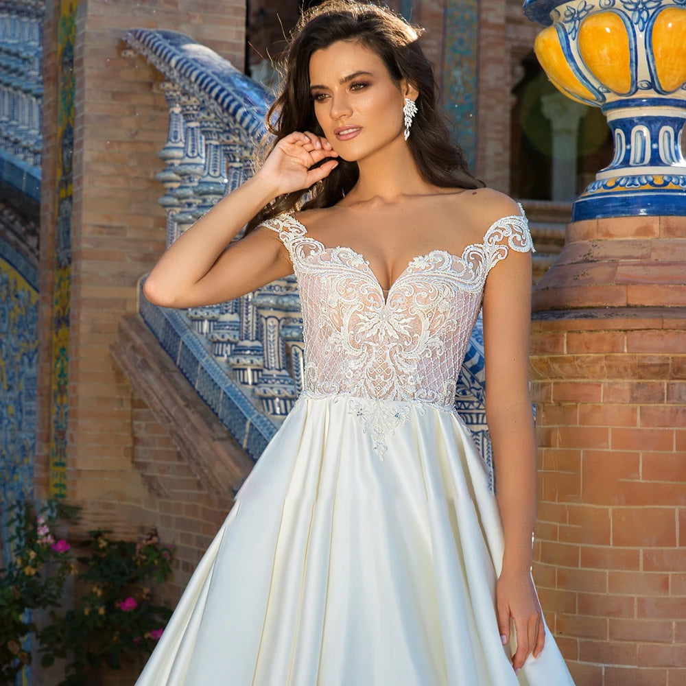 Front-facing portrait of a model in a luxury off-the-shoulder A-line wedding dress, focusing on the lace applique and elegant long-sleeve design.