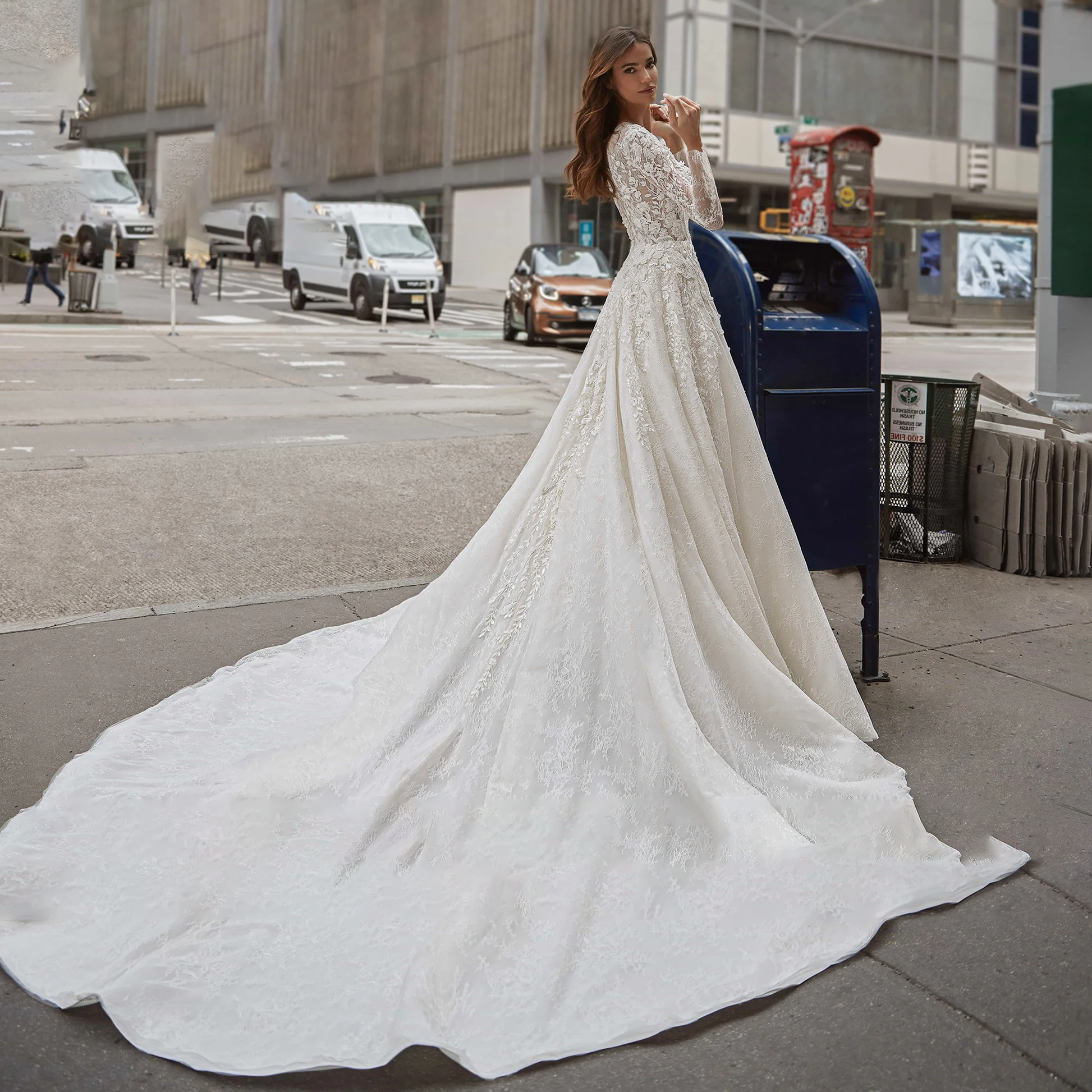 A back view of a bride walking down a city street in a luxury long-sleeve A-line wedding gown with a dramatic brush train and detailed sequinned beading.