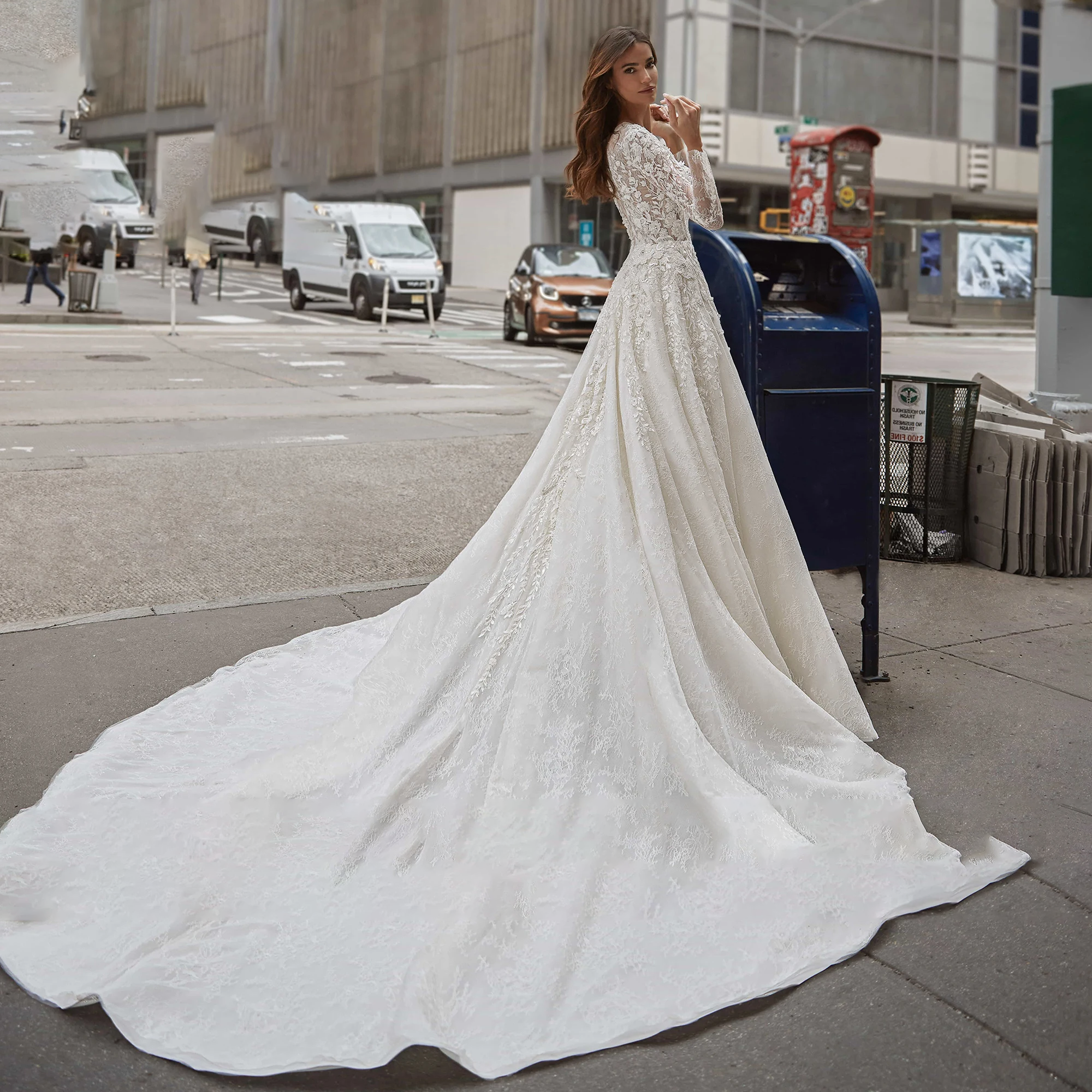 A back view of a bride walking down a city street in a luxury long-sleeve A-line wedding gown with a dramatic brush train and detailed sequinned beading.