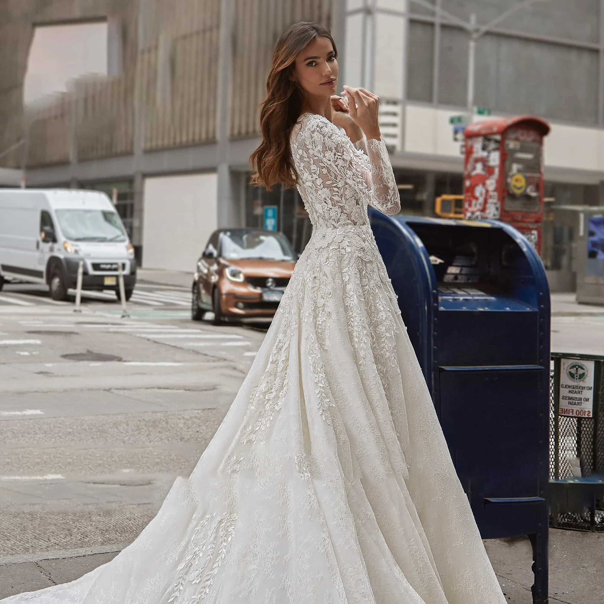 A profile shot of a bride posing in an A-line wedding dress with sequinned illusion long sleeves and a flowing skirt, set against a city backdrop.
