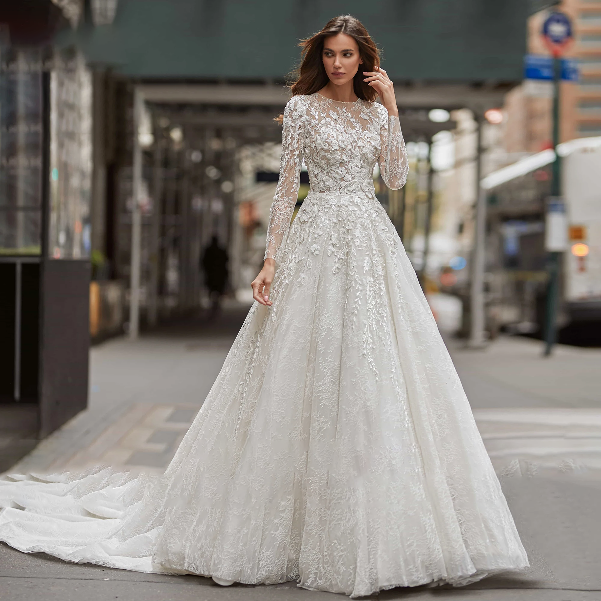 A portrait of a bride posing in a sophisticated A-line wedding gown, featuring long illusion sleeves and detailed sequinned beading on the bodice.