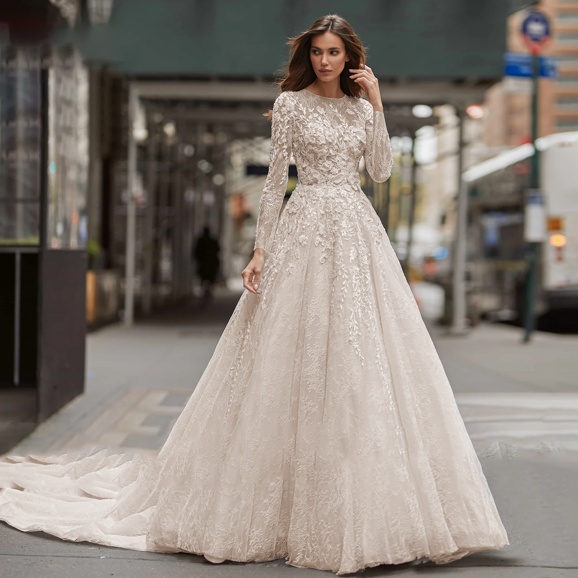 A side-angle view of a bride in an A-line wedding dress with long sleeves and a brush train, showcasing the luxurious sequinned illusion beading in an urban setting.