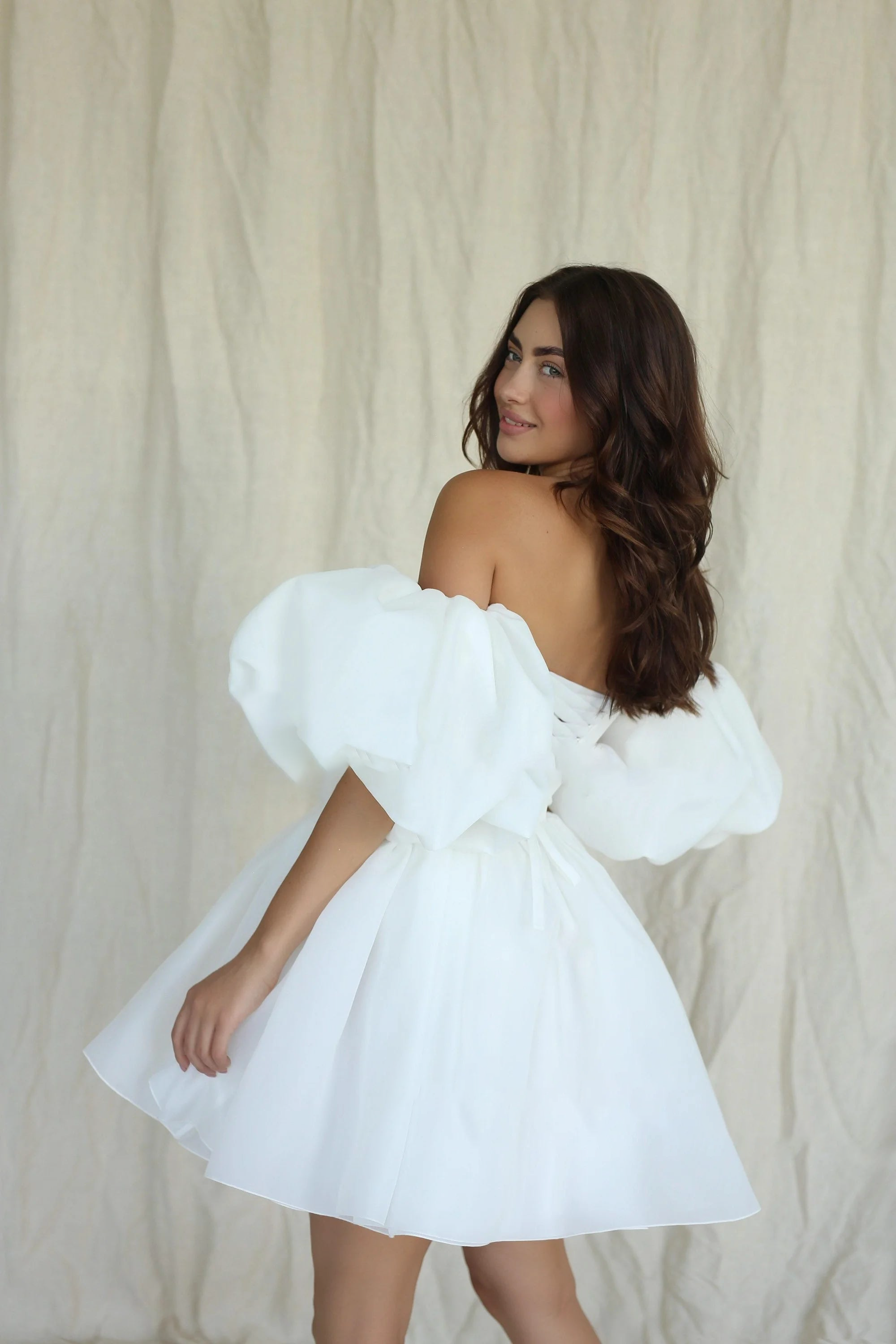 Over-the-shoulder rear view of a short off-the-shoulder organza wedding dress, highlighting the voluminous puff sleeves, low-cut back, and flared mini skirt silhouette.