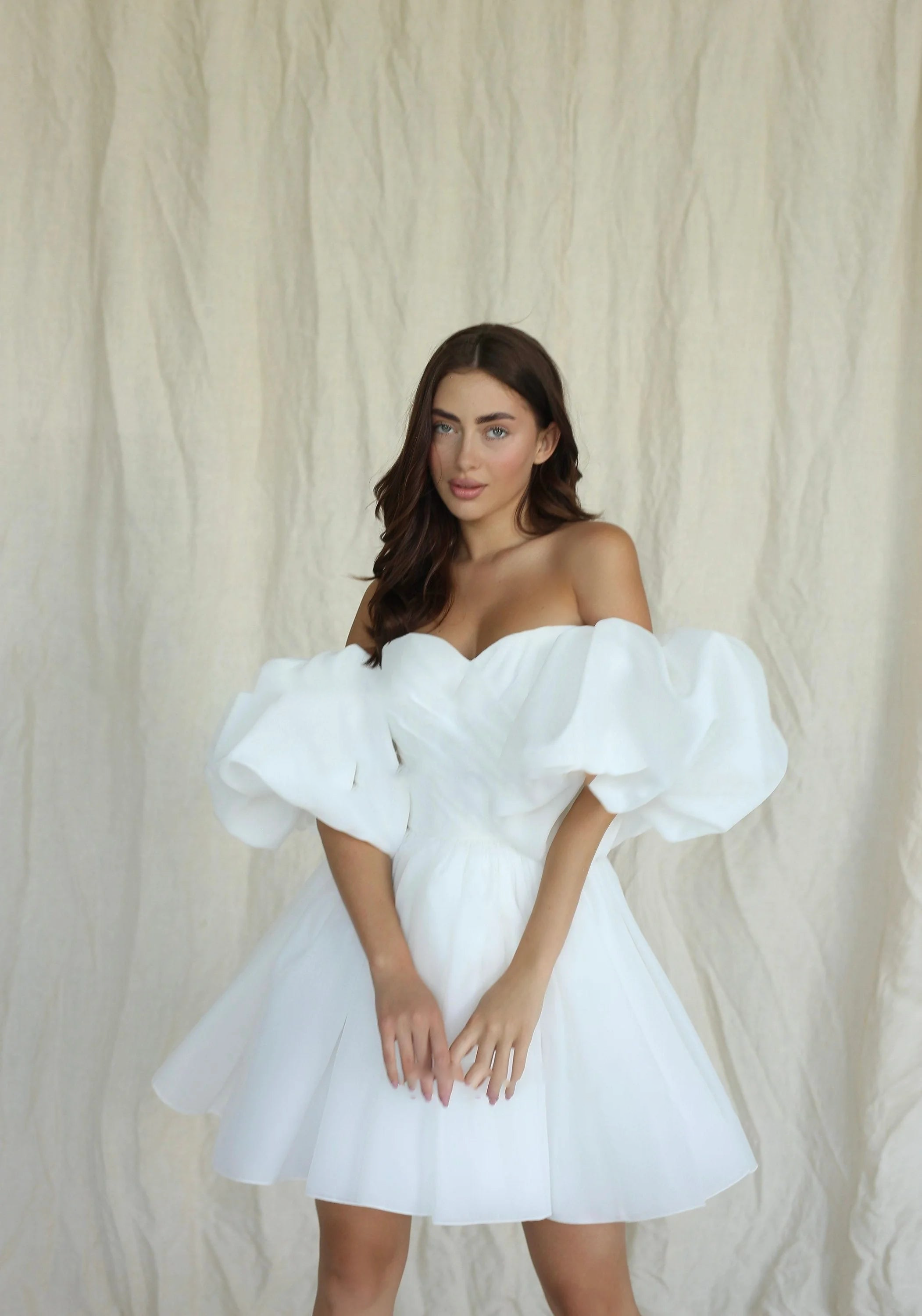 Half-length portrait of a bride wearing an elegant white organza mini dress with oversized detachable bubble sleeves and a draped sweetheart corset torso.