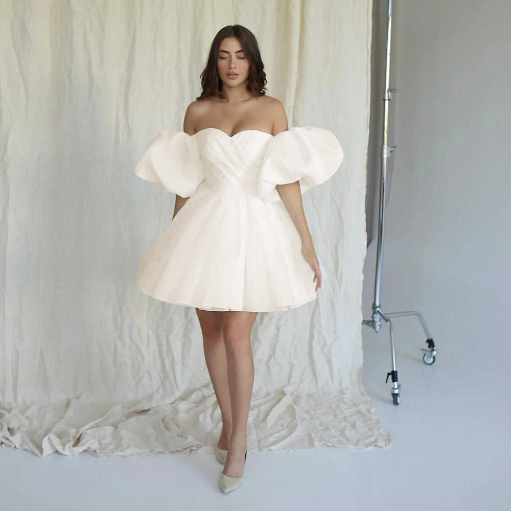 Short A-line organza rehearsal dinner dress in a soft ivory hue, showing off the architectural drapery of the sweetheart cups and voluminous off-shoulder puff sleeves.