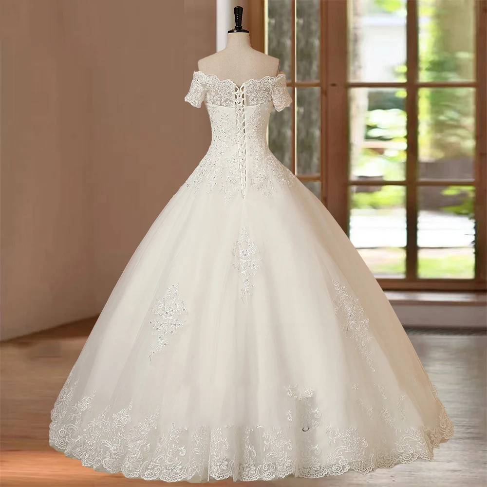 Back view of an A-line tulle wedding dress on a mannequin, featuring an adjustable lace-up corset back, sheer lace off-the-shoulder sleeves, and a sweeping skirt.