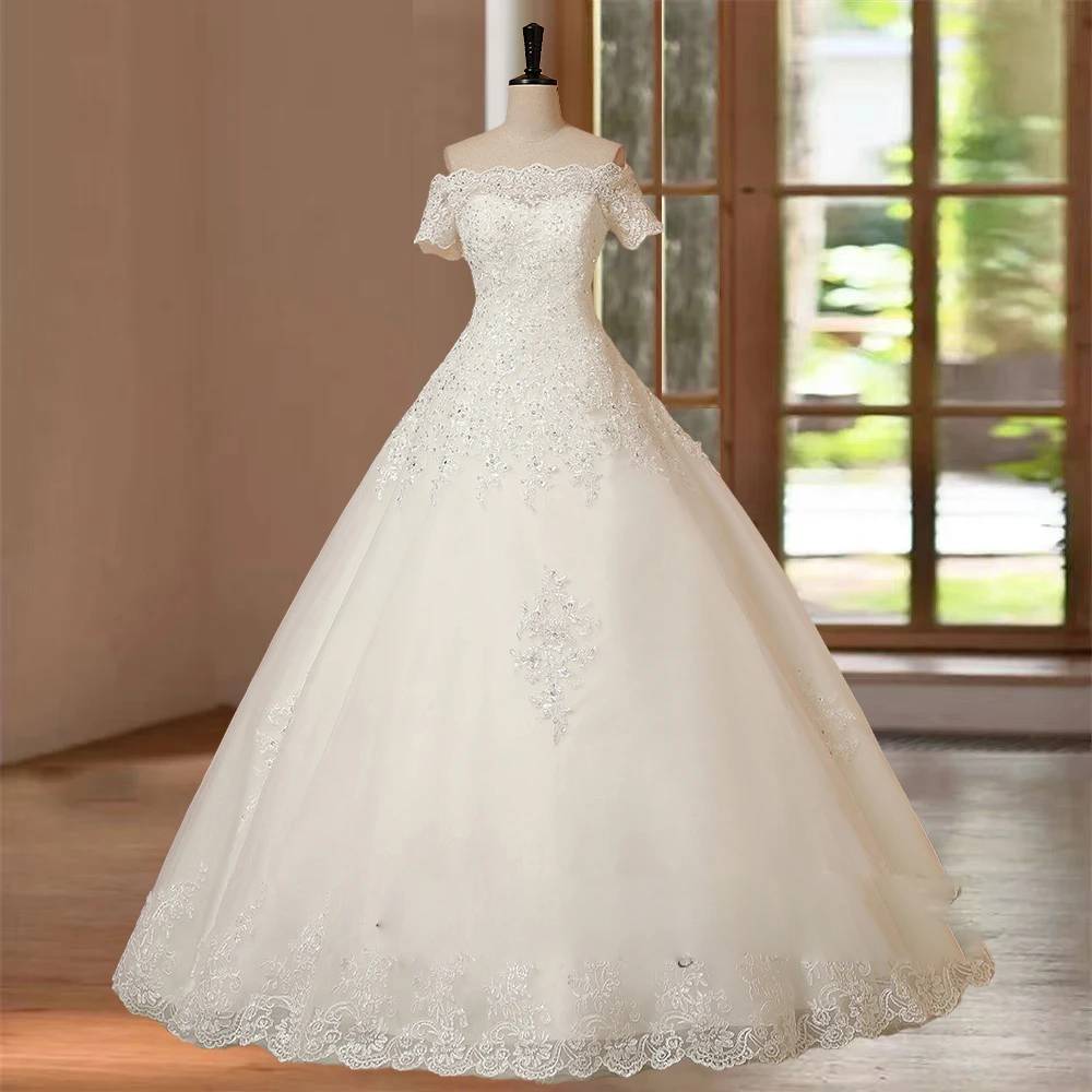 Standard front-facing studio shot of a white A-line short sleeve bridal gown with a sweetheart illusion neckline and detailed lace skirt trim.