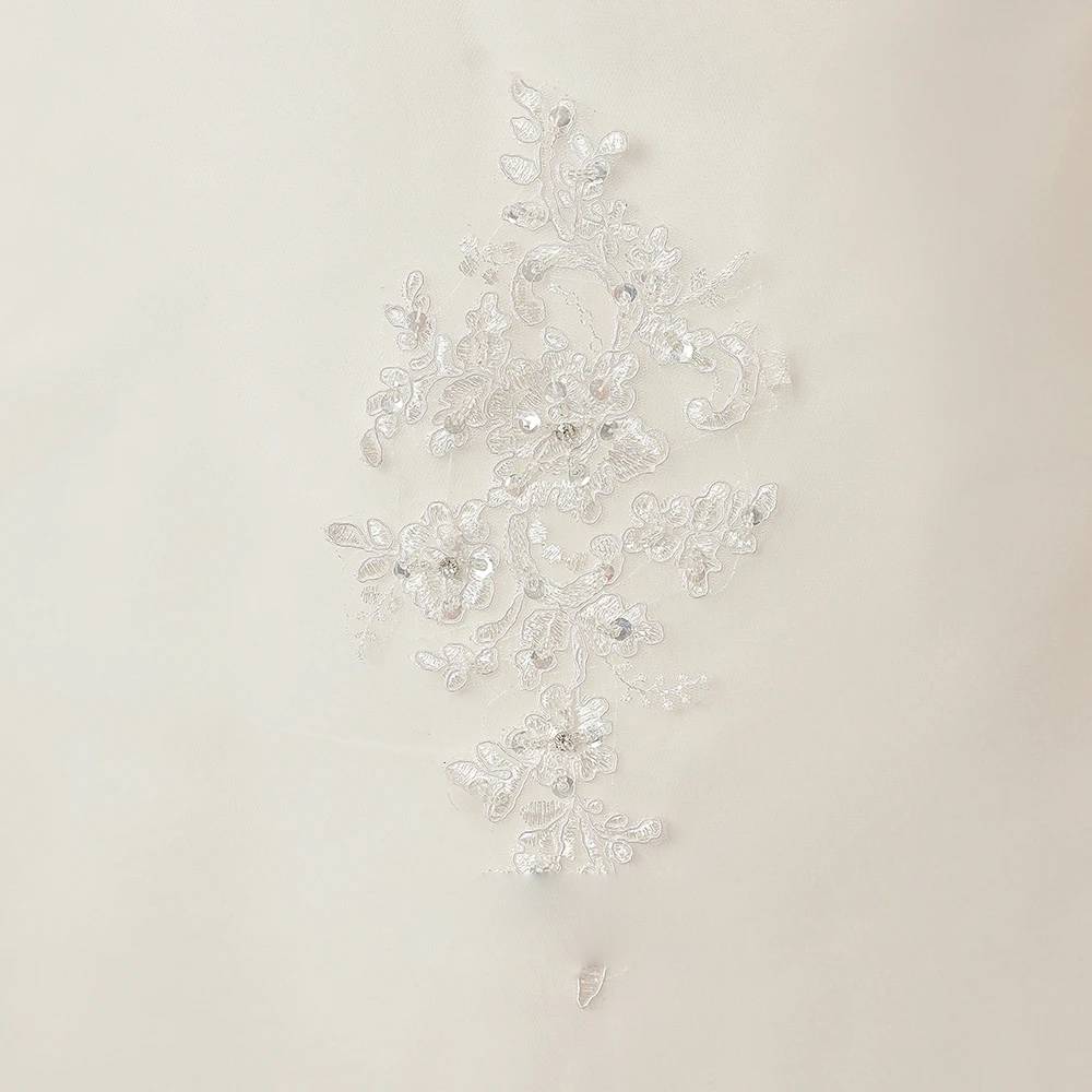 Extreme close-up of luxury bridal dress fabric detailing a hand-beaded floral lace applique with clear sequins and embroidery on soft white tulle.