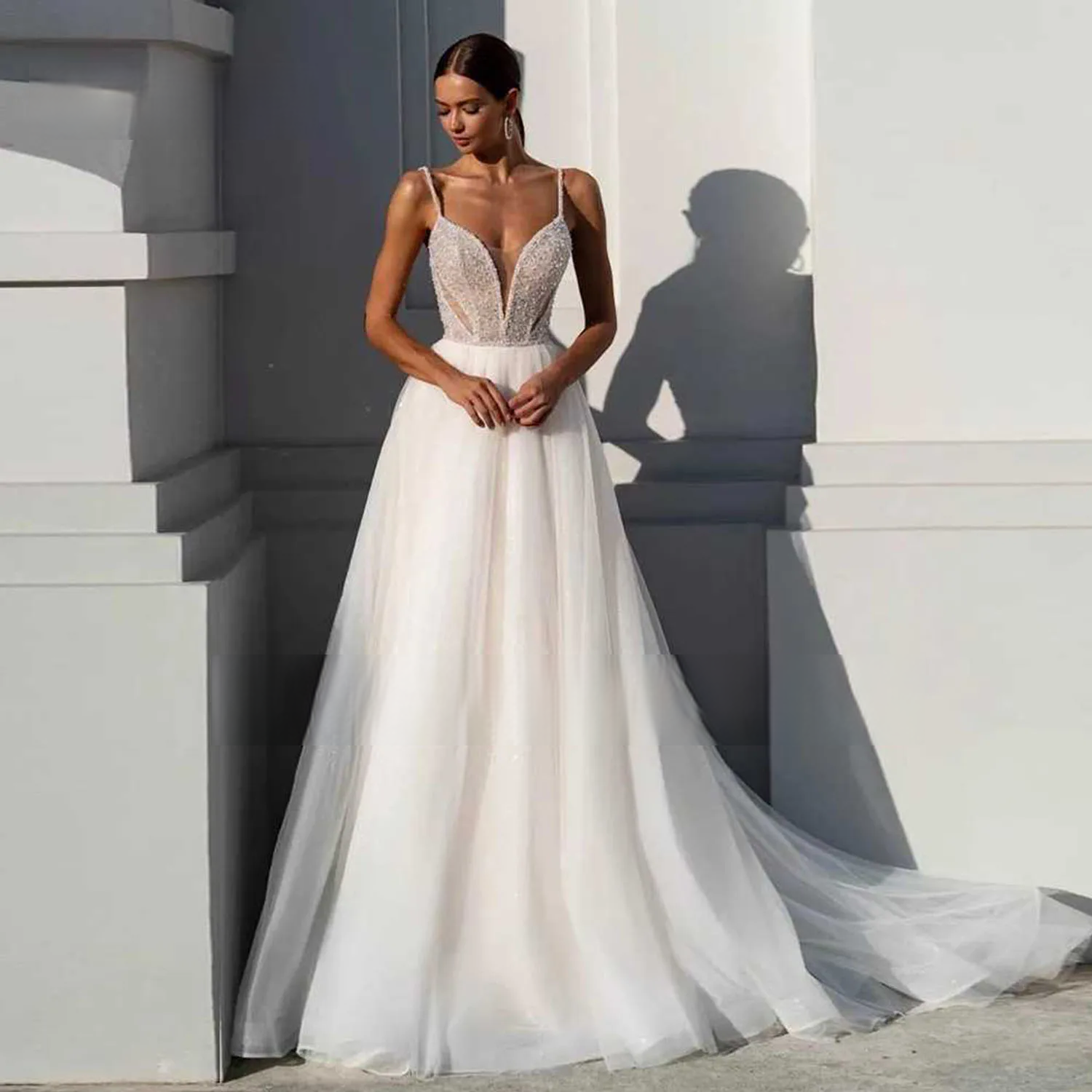 Beautiful bride modeling an A-line wedding dress with thin straps, a plunging sweetheart neckline, and a sweeping tulle skirt with a long train in a bright outdoor setting.