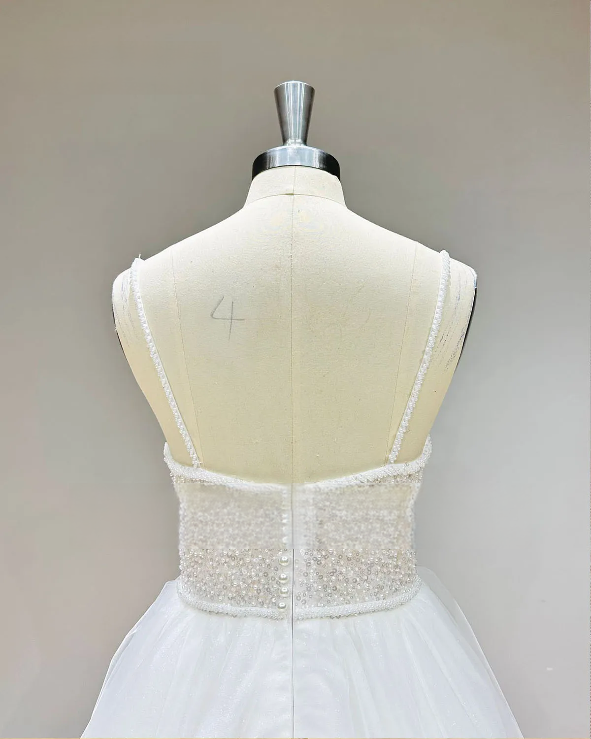 Rear perspective of the bridal gown bodice in highlighting the thin beaded straps and an elegant pearl button back closure.