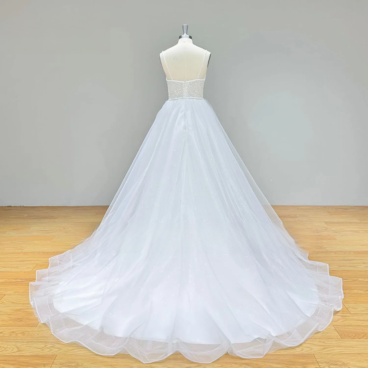 Wide rear view of the white A-line wedding dress in emphasizing the sophisticated backless silhouette and the expansive sweep of the cathedral-length tulle train.