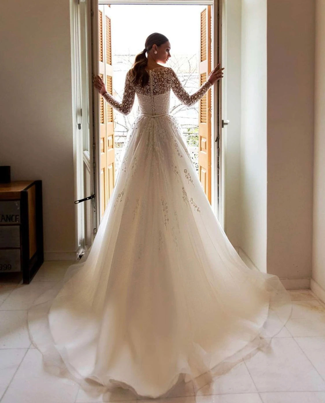 Rear view of an A-line bridal gown showcasing a button-up lace back, long sheer sleeves, and a full tulle skirt.