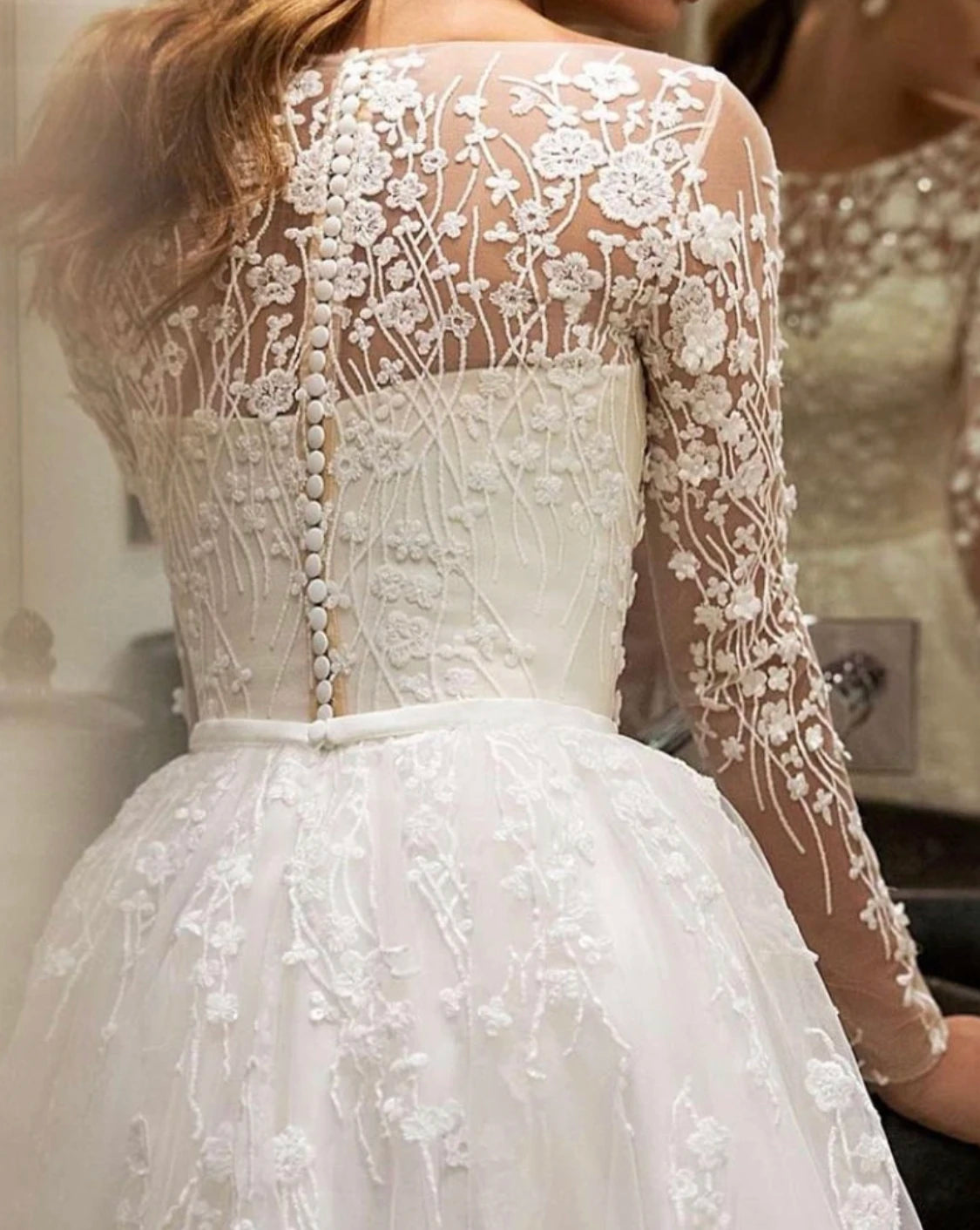 Close-up detail of the bodice on a champagne tulle wedding dress, highlighting fine floral lace embroidery and button accents.