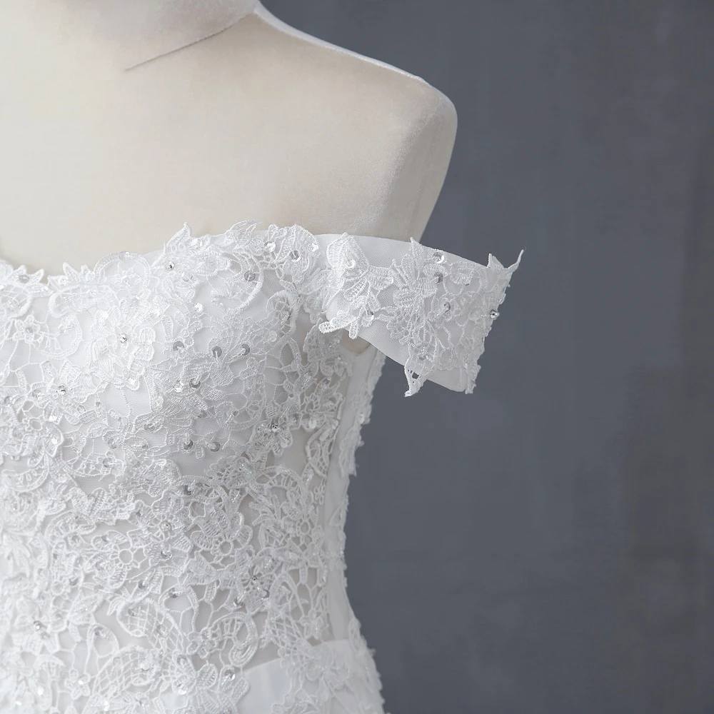Close-up detail of the intricate lace appliques and crystal embellishments on the boat neck sleeve of the bridal gown.