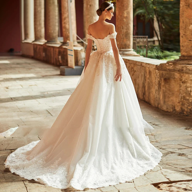 Back view of a stunning A-line wedding gown featuring a lace-up corset back and an expansive tulle train with delicate appliqué detailing.