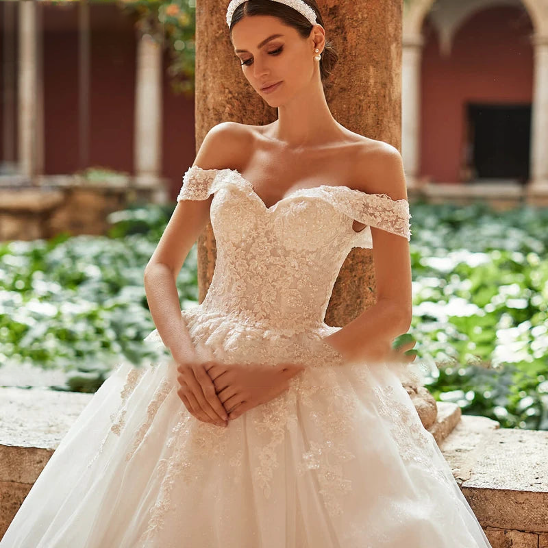 Close-up shot of a bride in an off-shoulder A-line bridal gown, focusing on the detailed floral lace appliqué and sweetheart bodice.