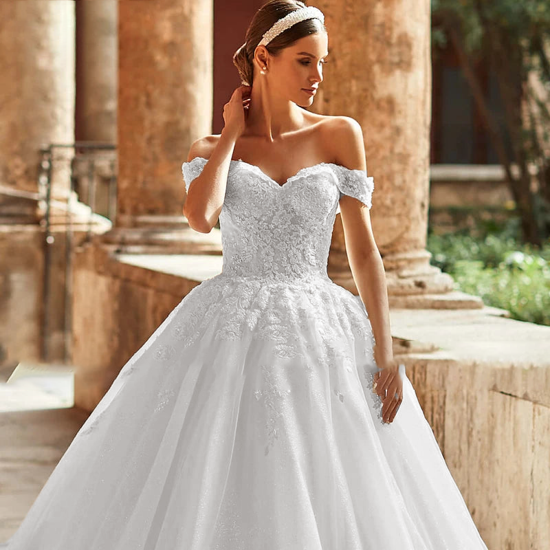 A model posing in an off-shoulder A-line bridal gown with a sweetheart neckline and exquisite floral appliqué design.