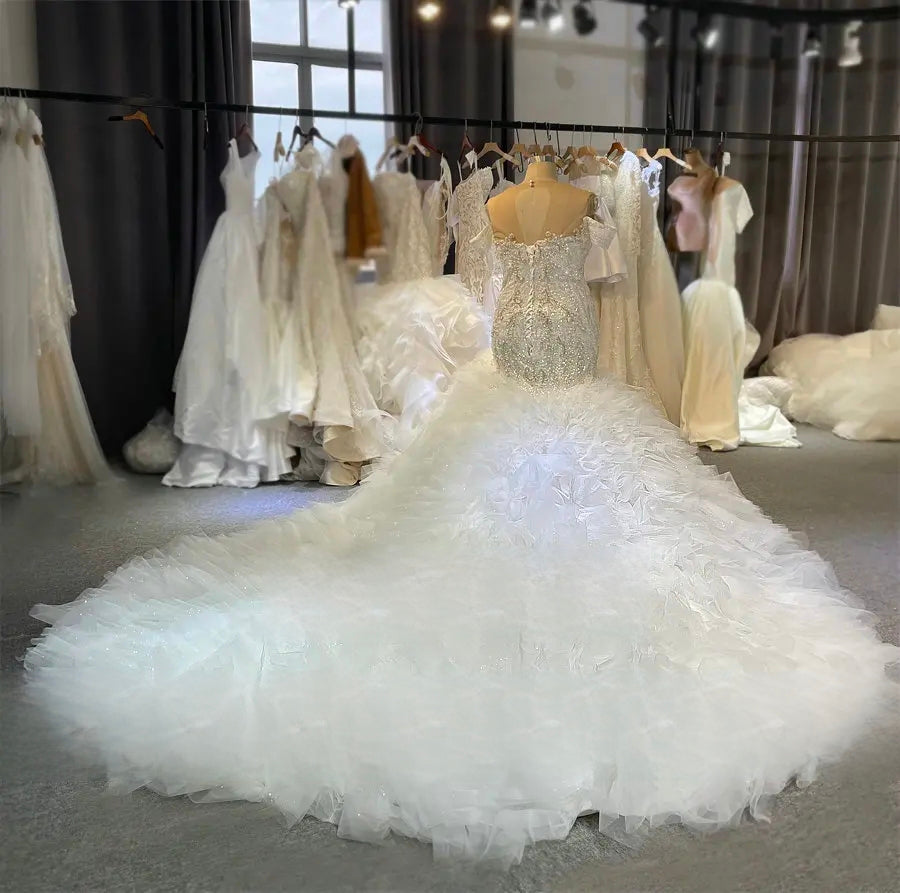 Rear view of the luxury mermaid wedding dress on a mannequin, displaying the corset lace-up back and the expansive, multi-tiered ruffled tulle train in a bridal studio.