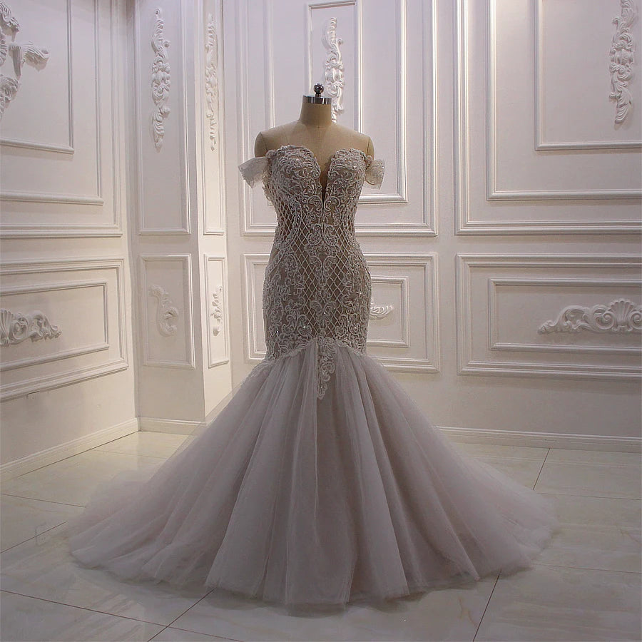Close-up front view of an African off-shoulder mermaid wedding dress on a mannequin, showcasing the intricate geometric lace patterns and deep sweetheart neckline.