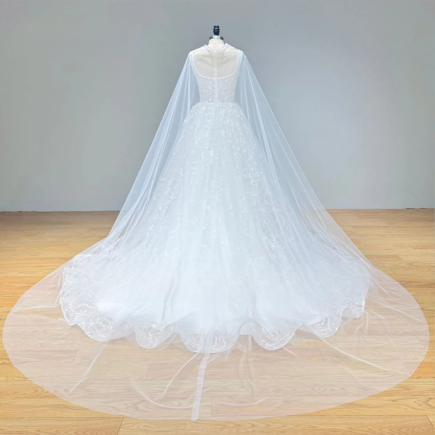 Rear view of the shiny beaded wedding dress on a mannequin, emphasizing the expansive cathedral-length train and the sheer back of the decorative cape.