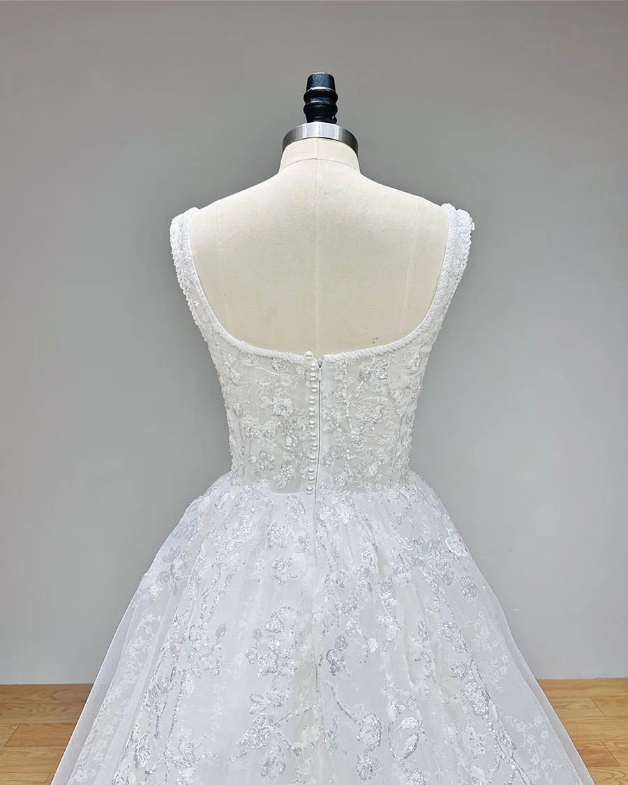 Close-up back view of the wedding dress (without cape), showing the elegant U-shaped open back with a traditional row of bridal buttons and floral lace appliques.