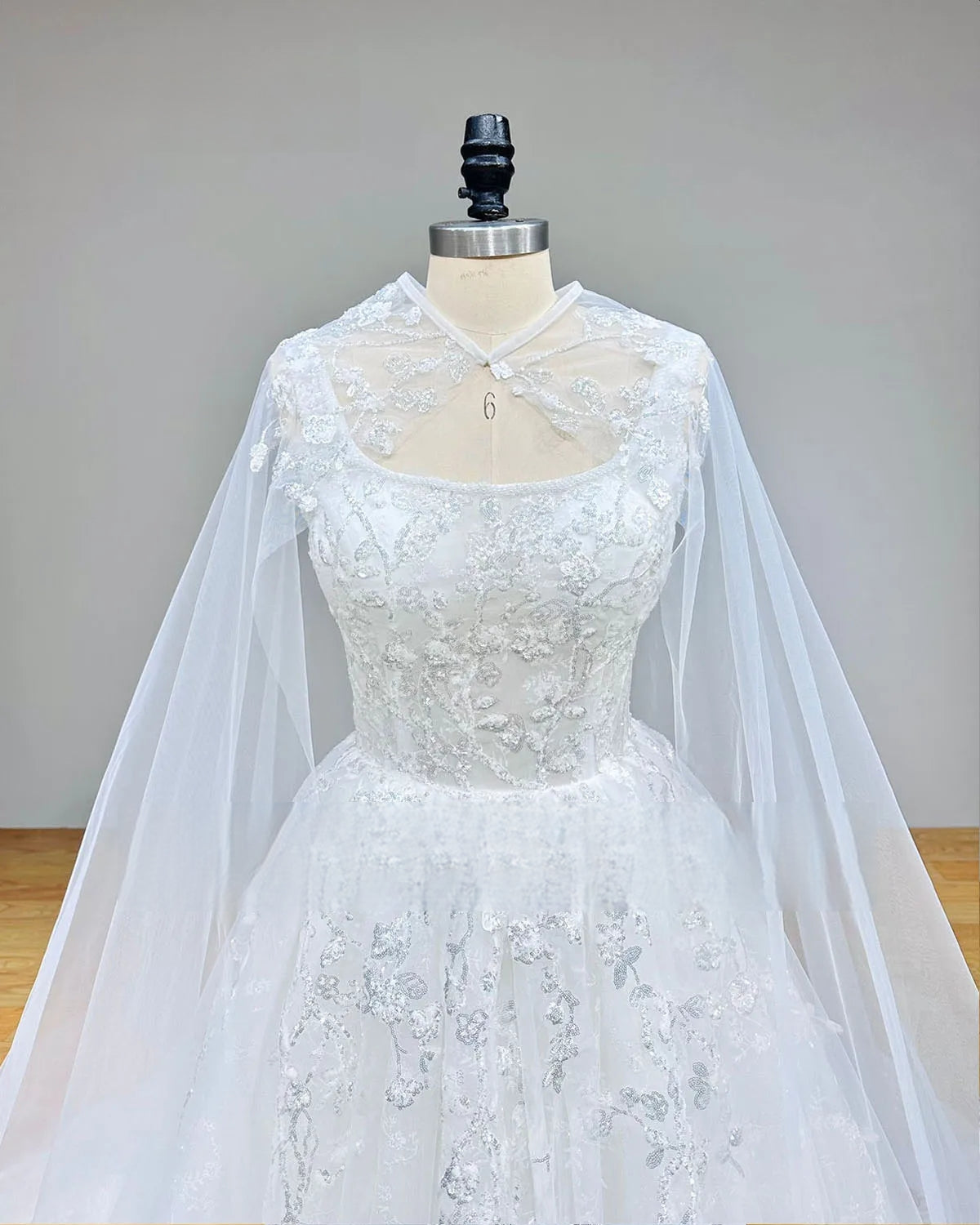 Close-up front bodice detail of the white beaded wedding dress, showcasing the sweetheart neckline beneath a sheer high-neck cape with shimmering silver sequin designs.