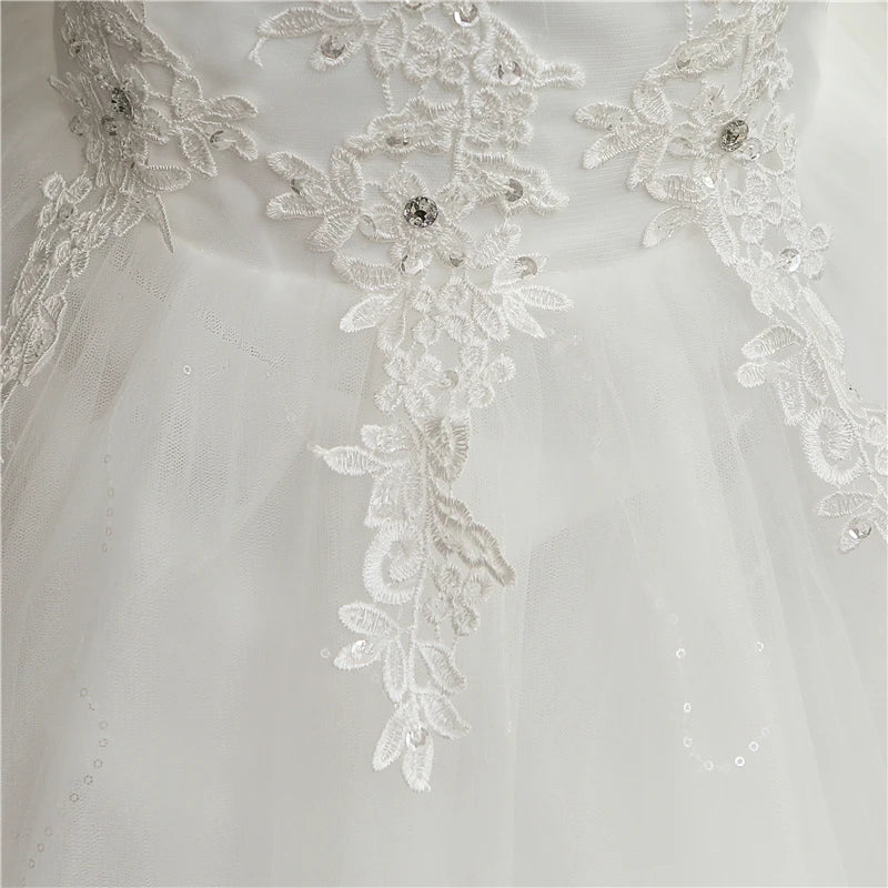 Intricate close-up detail of the scalloped floral lace trim and delicate embroidery along the hemline of the vintage long-sleeve ball gown wedding dress train.