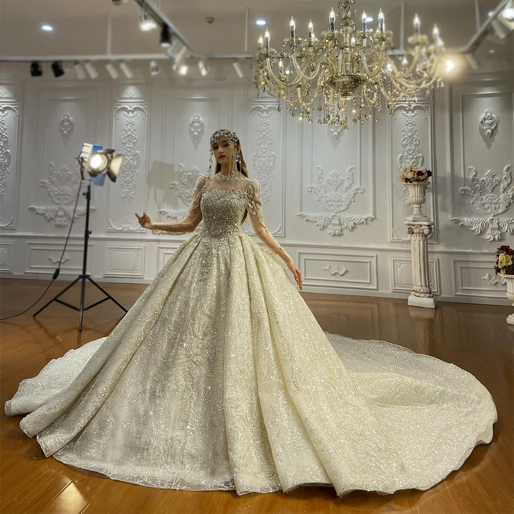 High-end 2025 bridal fashion featuring a silver glitter ball gown with long sleeves and a grand princess silhouette, complete with an ornate crystal headpiece.