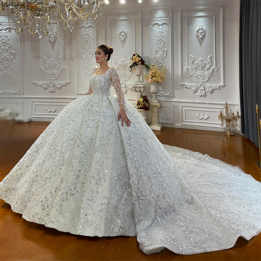 Full side-profile of a model wearing a luxury ball gown wedding dress with a dramatic removable long train, featuring intricate silver hand-beading and elegant long sleeves.
