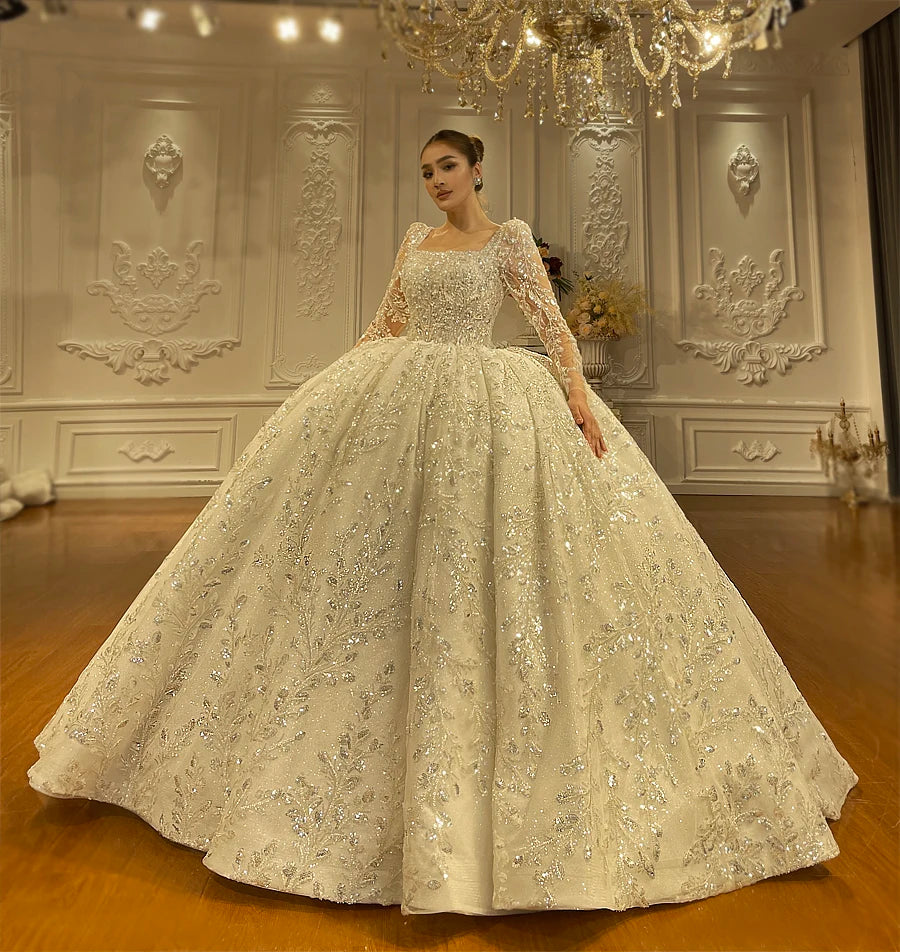Frontal view of an elegant bridal ball gown featuring a modern square neckline, shimmering crystal beading, and a voluminous flared skirt.