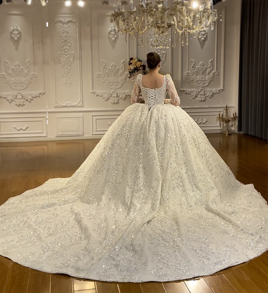 A wide-angle back perspective of the dramatic wedding dress, emphasizing the expansive, sparkling removable train spread across a showroom floor.