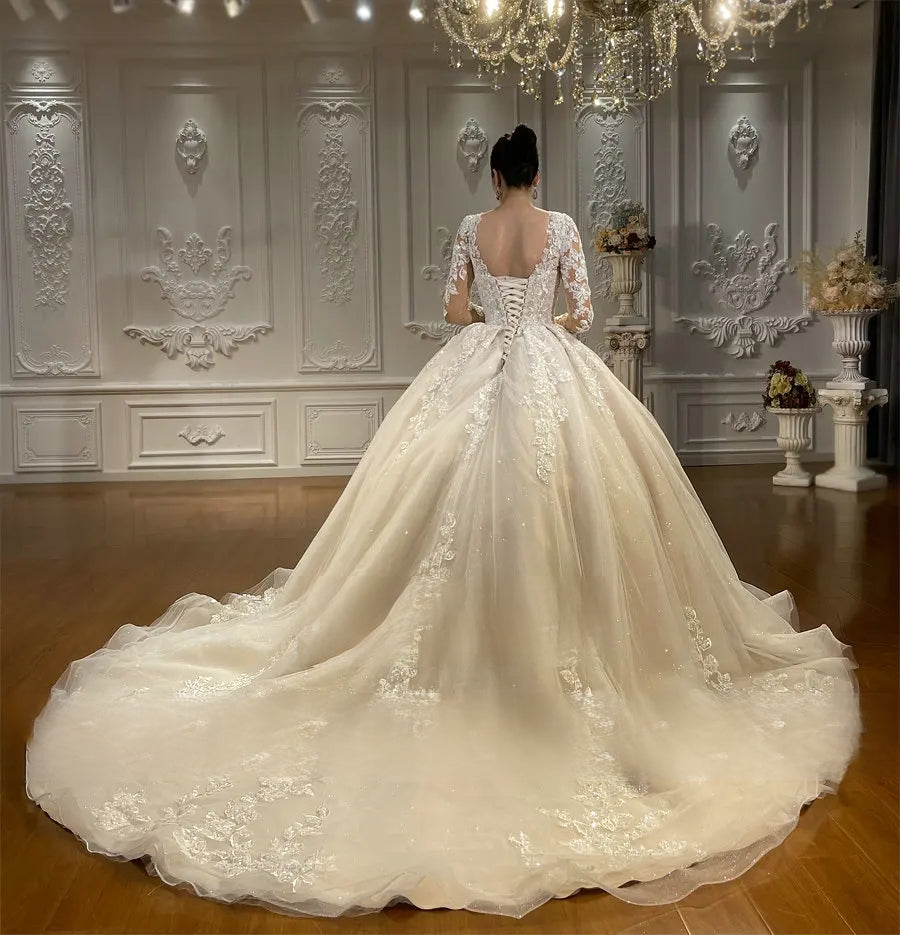 Detailed back perspective of a beach style bridal gown showing the elegant low-back cut, corset closure, and the expansive flow of the shimmering tulle long train.