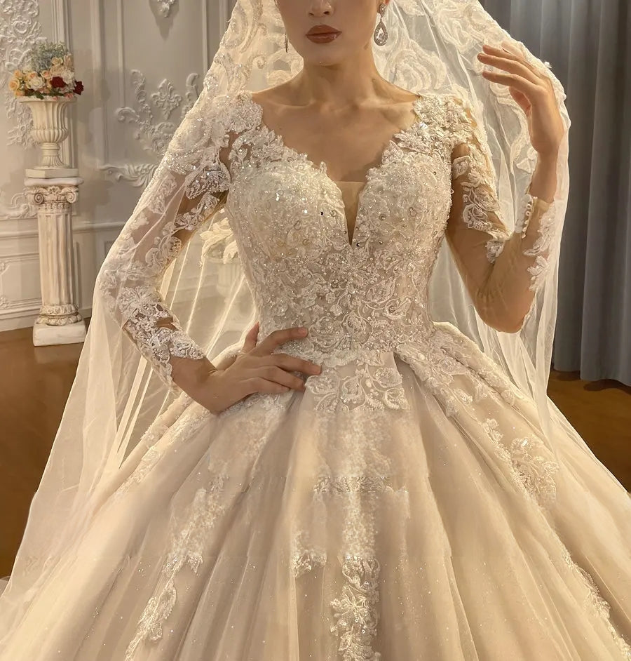 Close-up detail of a luxury wedding dress bodice, featuring hand-beaded lace embroidery, a plunging neckline, and sophisticated floral patterns on sheer long sleeves.