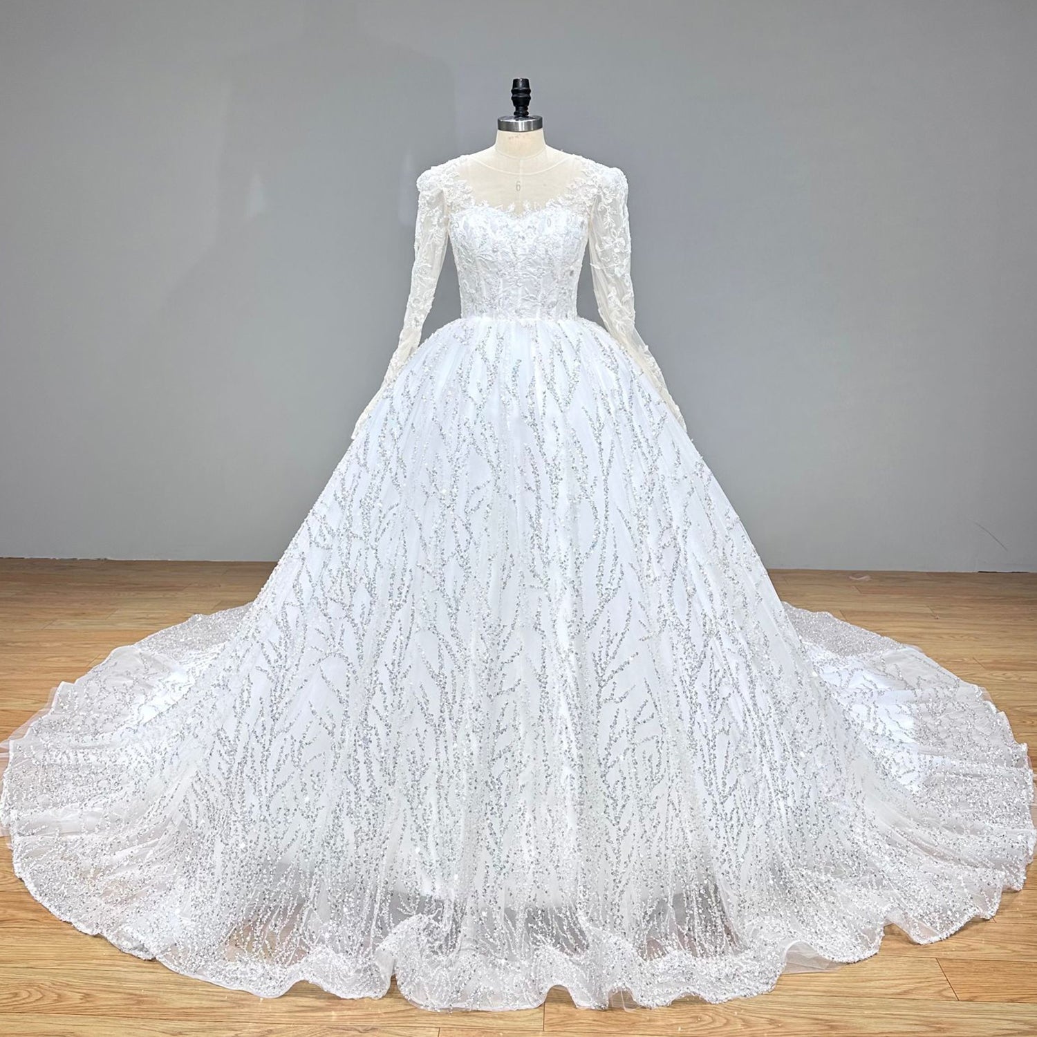 Front studio view of a premium white long sleeve beaded ball gown wedding dress with an expansive branch-patterned sequined skirt.