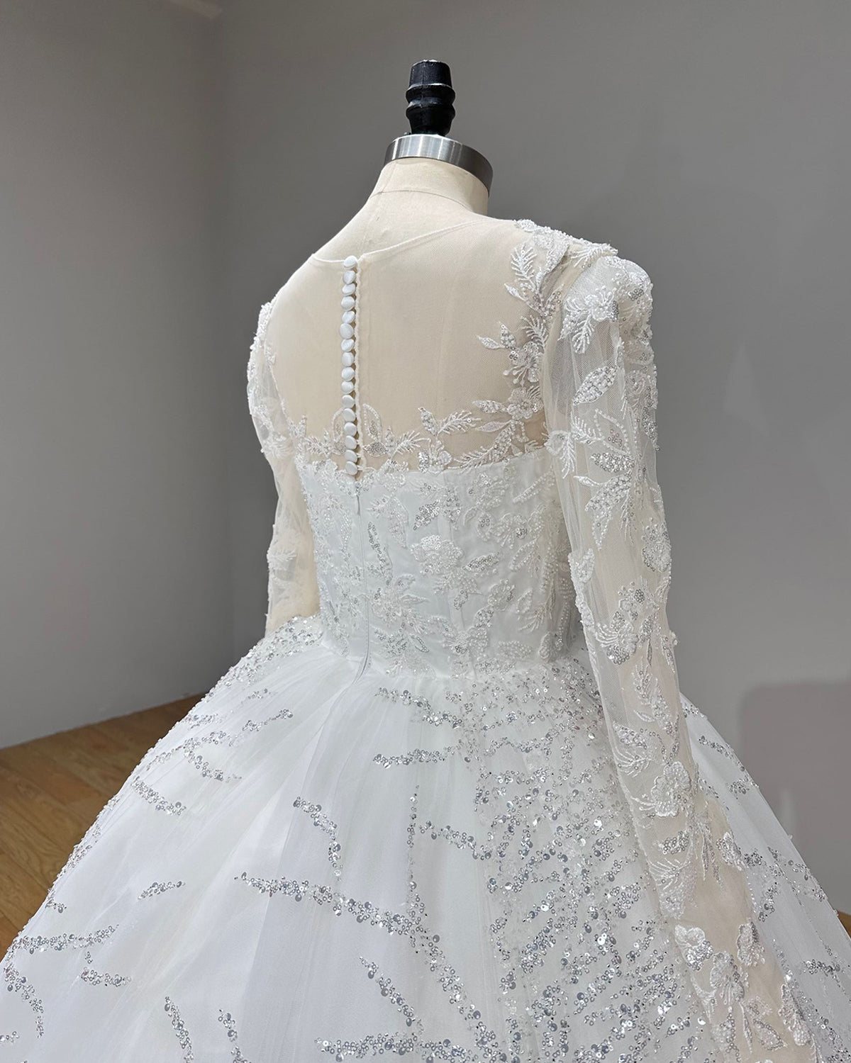 Close-up side back view of a bridal gown showcasing a sheer illusion see-through back with delicate floral lace embroidery and fabric-covered buttons.