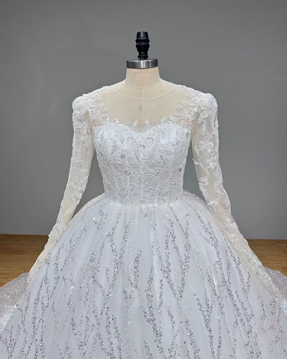 Front close-up view of a bridal bodice highlighting an illusion scoop neckline, sheer long sleeves, and intricate crystal beadwork.
