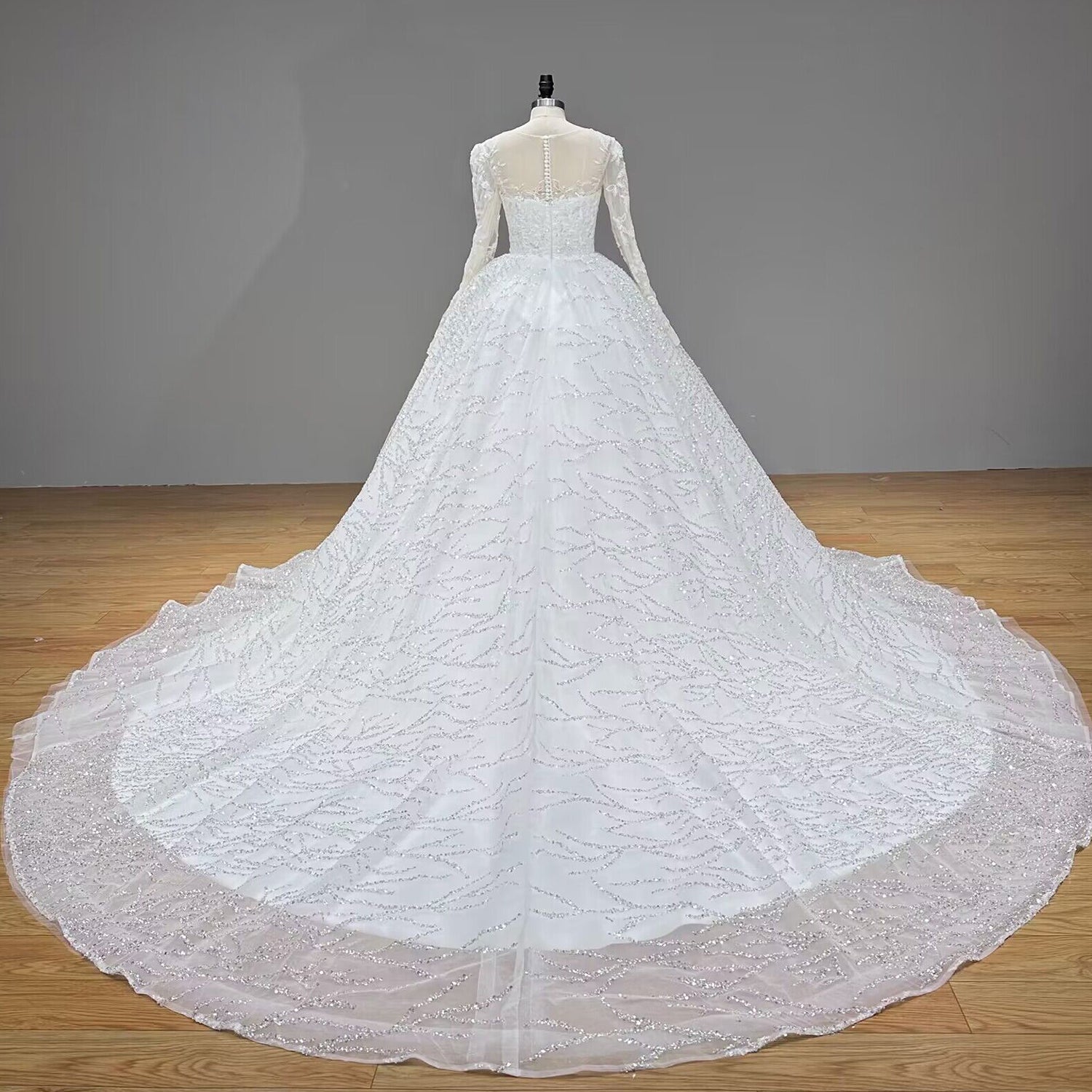 Full-length back studio view of a white beaded ball gown wedding dress on a mannequin, emphasizing a dramatic sweeping glitter tulle train.