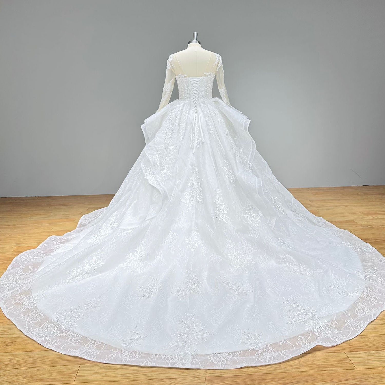 Back view of a vintage long-sleeve wedding dress showcasing a classic lace-up corset back, illusion tulle shoulders, and a sweeping lace-bordered train.
