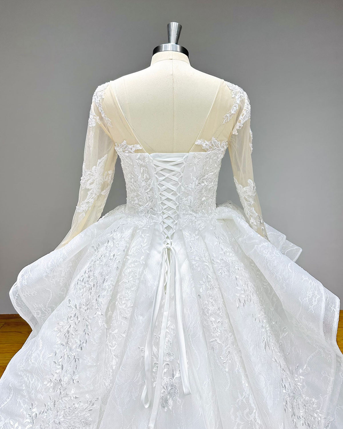 Back view of a vintage long-sleeve wedding dress showcasing a classic lace-up corset back, illusion tulle shoulders, and a sweeping lace-bordered train.