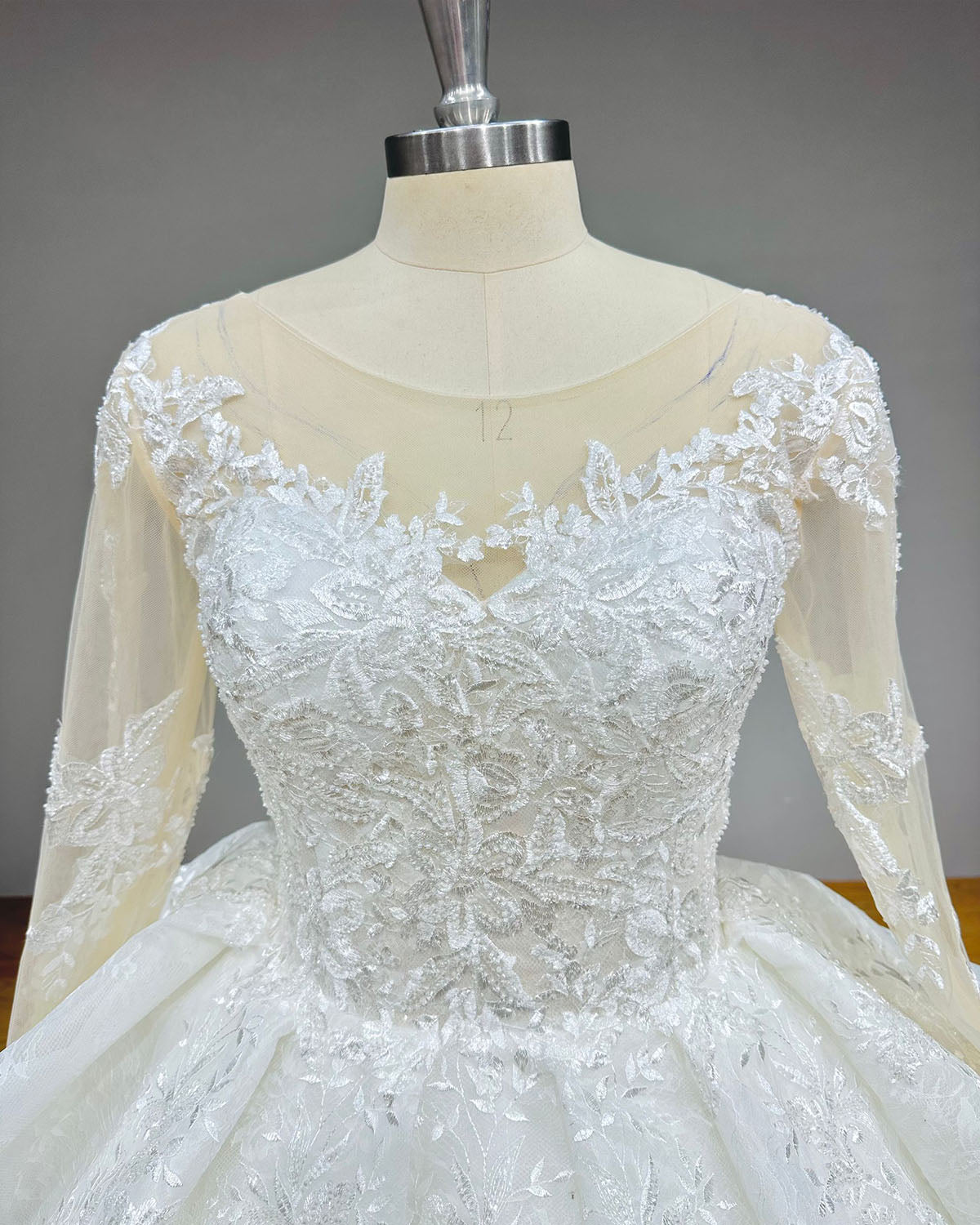 Close-up of the back of a bridal gown highlighting the adjustable satin lace-up corset closure, sheer illusion sleeves, and delicate floral appliques.