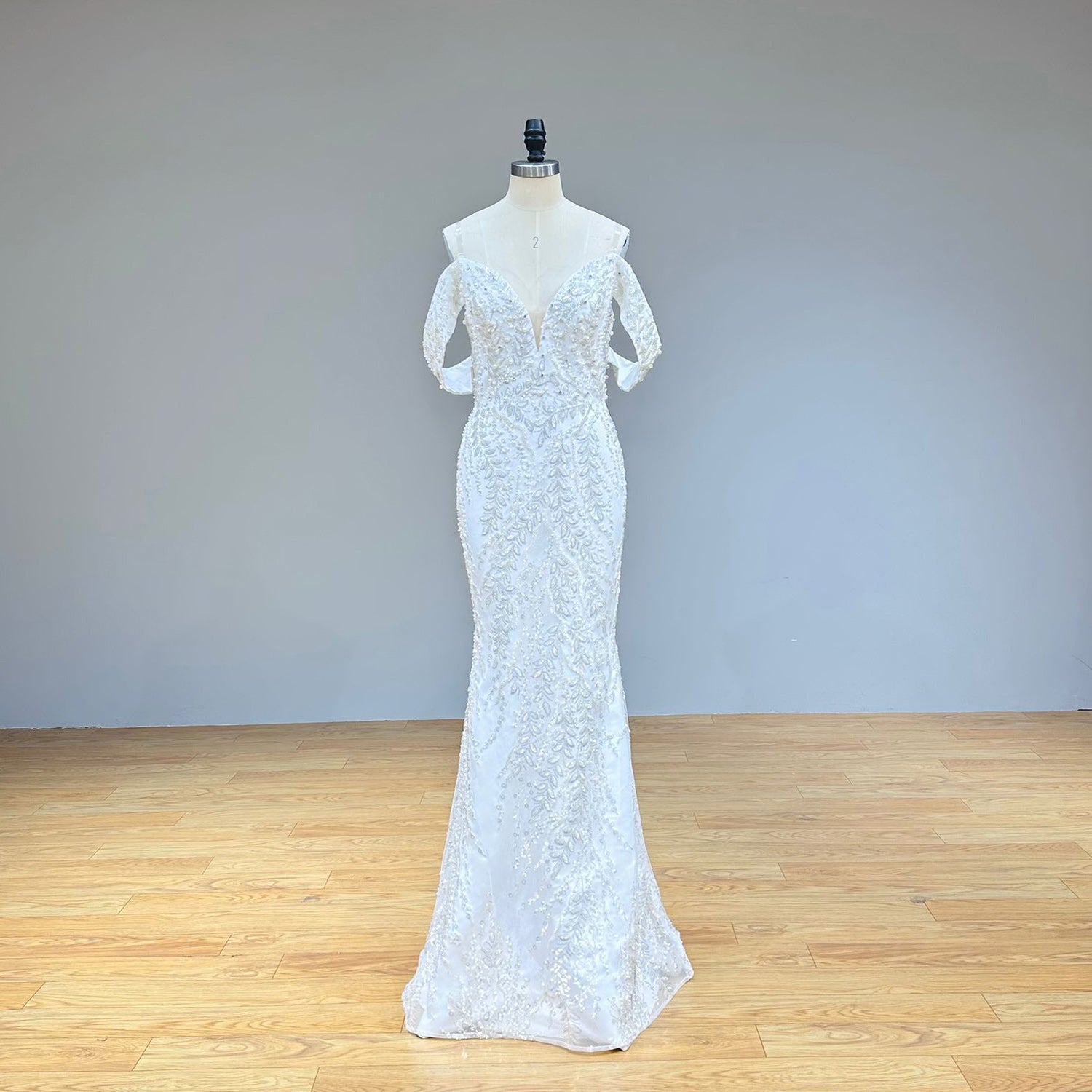 Full front view of a beaded lace mermaid wedding dress on a mannequin in a studio hallway, highlighting the fitted silhouette and the added volume of the detachable train.