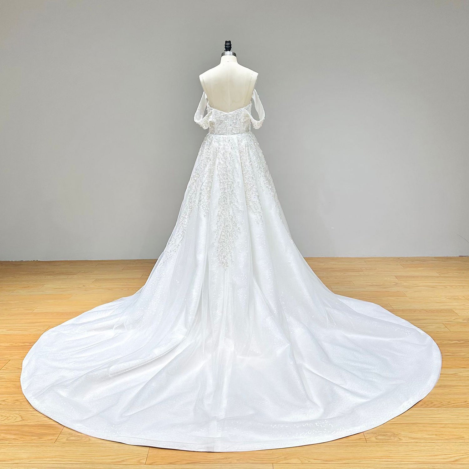 Full back view of an elegant mermaid wedding dress on a mannequin, displaying the sheer lace back detail, corset lace-up, and the sweeping detachable train.