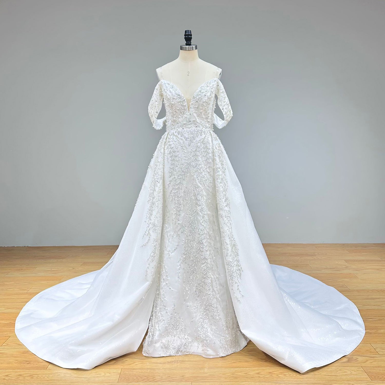 Full front studio view of a beaded lace mermaid wedding dress on a mannequin, capturing the form-fitting silhouette and the dramatic flare of the detachable train.